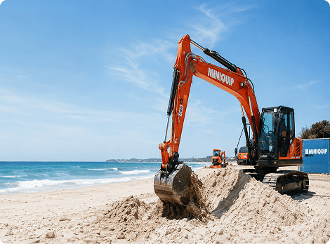 Miniquip hire mini skid steer loader working on sandy beach, ideal for construction and landscaping projects near water.