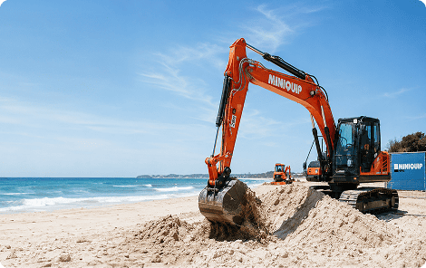 Miniquip hire mini excavator working on sandy beach for construction or landscaping projects.