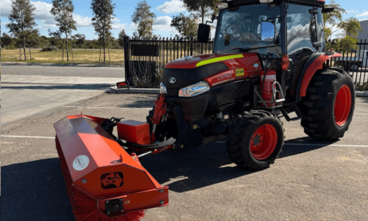 Red and black Miniquip hire tractor with sweeping attachment on a paved surface, ideal for construction and landscaping projects.
